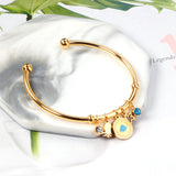 Gold bangle with two diamonds of different colors and a charm with a scallop on the door of the discus.