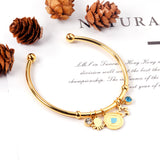 Gold bangle with two diamonds of different colors and a charm with a scallop on the door of the discus.